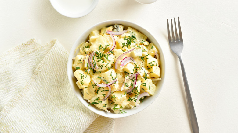 Potato salad with egg, pickle, red onion with mayonnaise and yogurt dressing in bowl on light background. Top view, flat lay