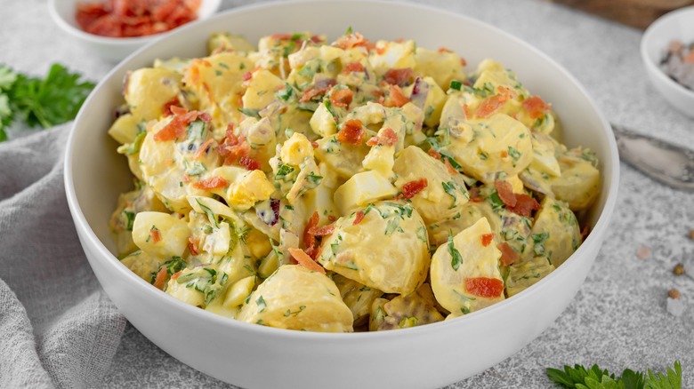 Salad of potatoes, eggs, bacon, and fresh herbs with mayonnaise and yogurt dressing in a bowl on a gray concrete background