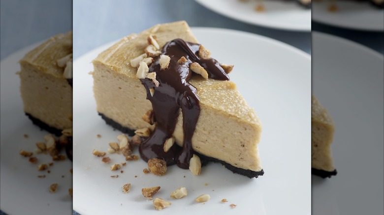 A slice of peanut butter pie drizzled with chocolate sauce and peanuts on a white plate