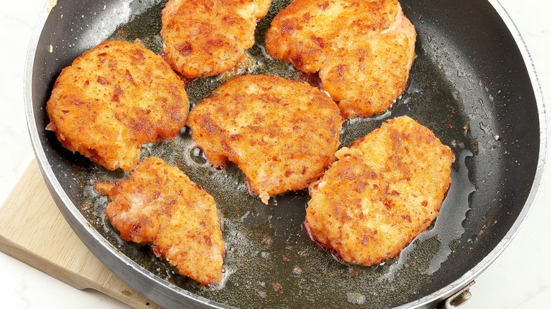 Pretzel-crusted chicken cutlets frying in oil in a dark-coated pan