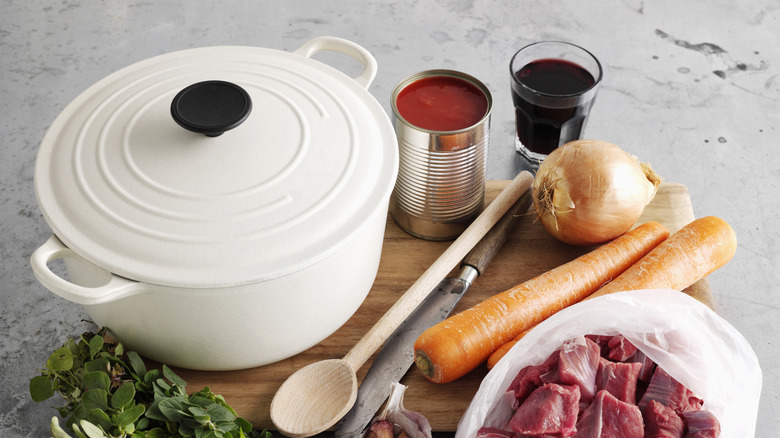White Dutch oven next to root veggies and cubed meat