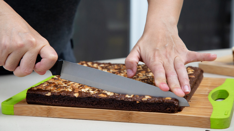 Someone cutting brownies on a wooden cutting board
