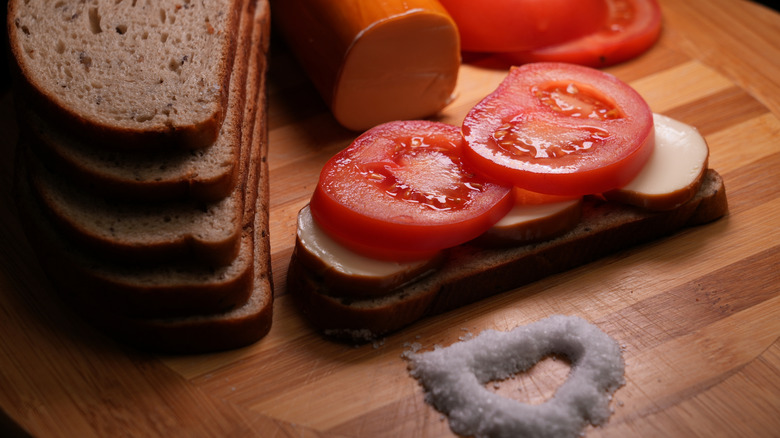 Two tomato slices on sliced bread on a cutting board neatr a pile of salt.