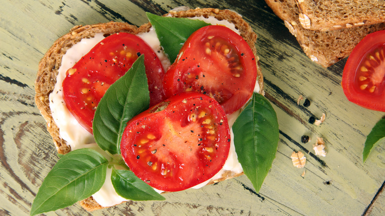An open-faced sandwich with ripe sliced tomatoes, mozzrella, and basil photographed from above.