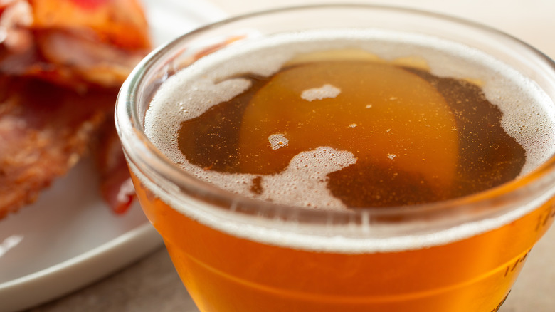 a closeup view of rendered bacon fat with bacon in the background
