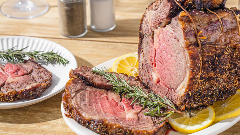 Prime rib roast, partially sliced, and served with fresh rosemary and lemon