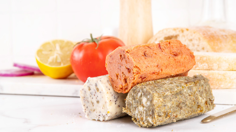 Three cylinders of compound butter stacked atop one another with tomato and lemon in background