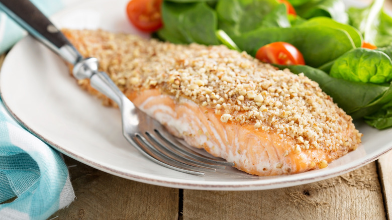 Nut-crusted salmon on white plate with salad and fork.