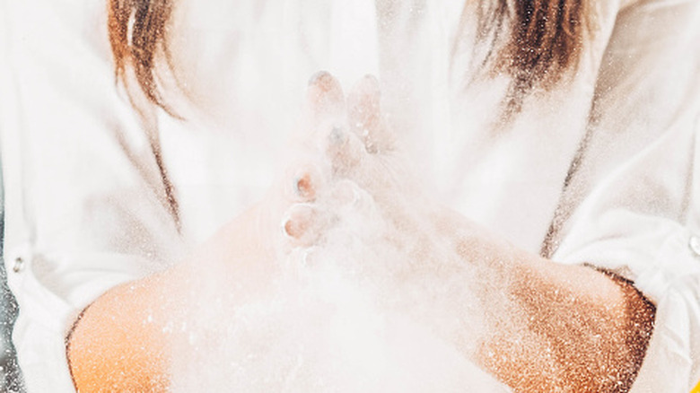 A close-up of a woman clapping her hands together, dusting flour all over