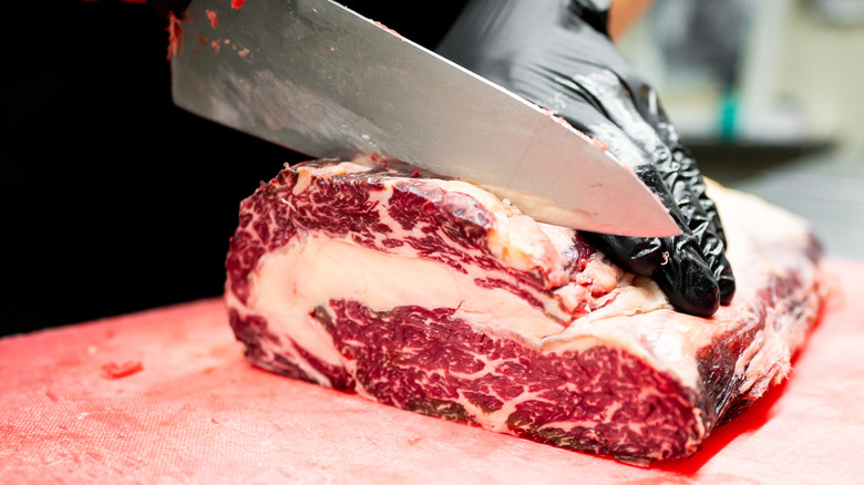 A hand wearing gloves cutting a beautifully marbled piece of meat with a knife