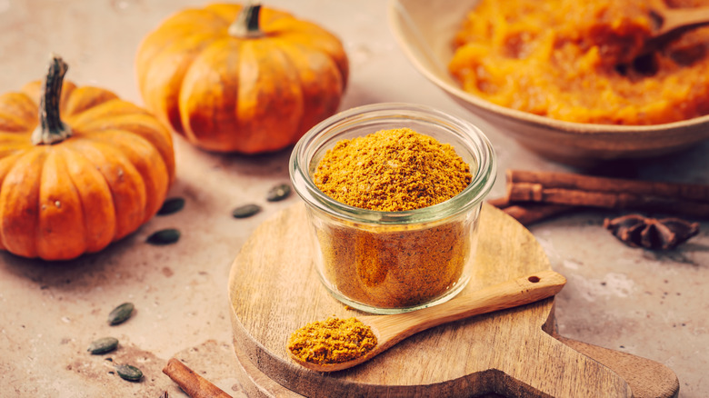 pumpkin pie spice in a glass cup surrounded by pumpkins
