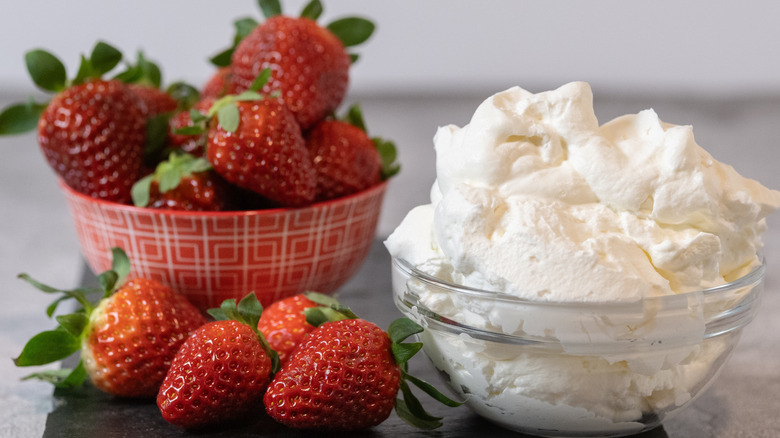 bowl of whipped cream next to strawberries