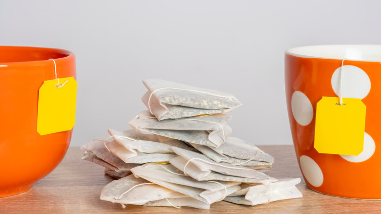 Several tea bags piled in between two orange mugs that feature yellow tea bag labels hanging over the edge.