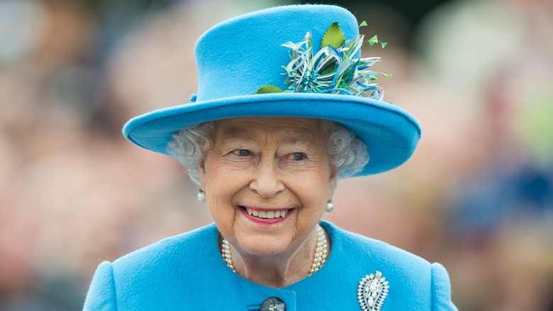 Queen Elizabeth smiling in a blue hat with feathers