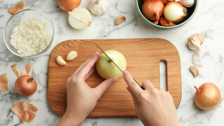 Top view of hands cutting an onion on a wooden board.