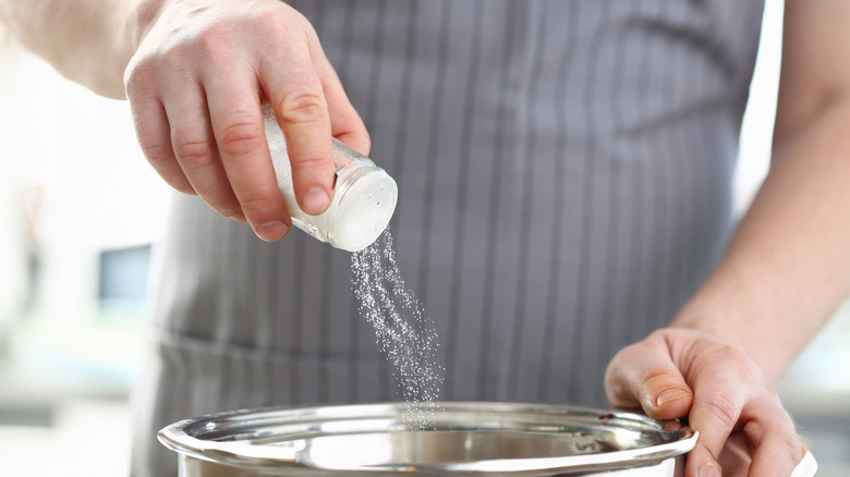 person sprinkling salt into pot