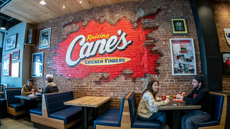 Interior of a Raising Cane's restaurant with logo and diners eating in booths