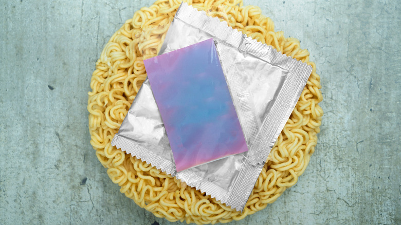 An unpackaged, dry ramen cake on a grey tabletop, with seasoning packets on top.