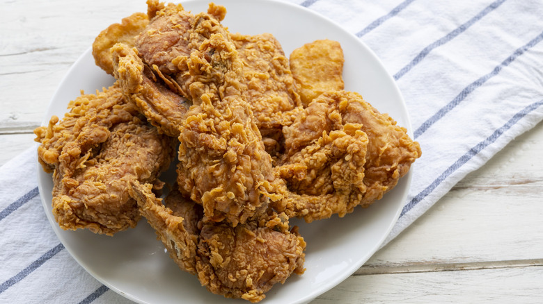 A plate of golden brown fried chicken over a tea towel on a white, wooden table.