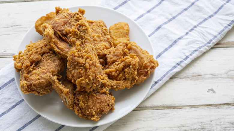 A plate of golden brown fried chicken over a tea towel on a white, wooden table.