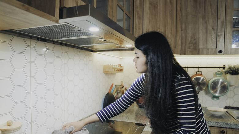 A woman cleans a stovetop under a range hood