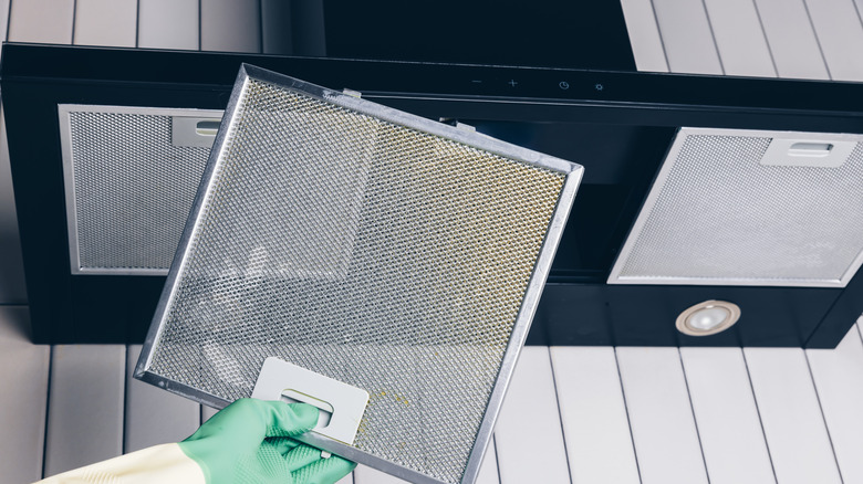 A hand removes a range hood filters to clean it
