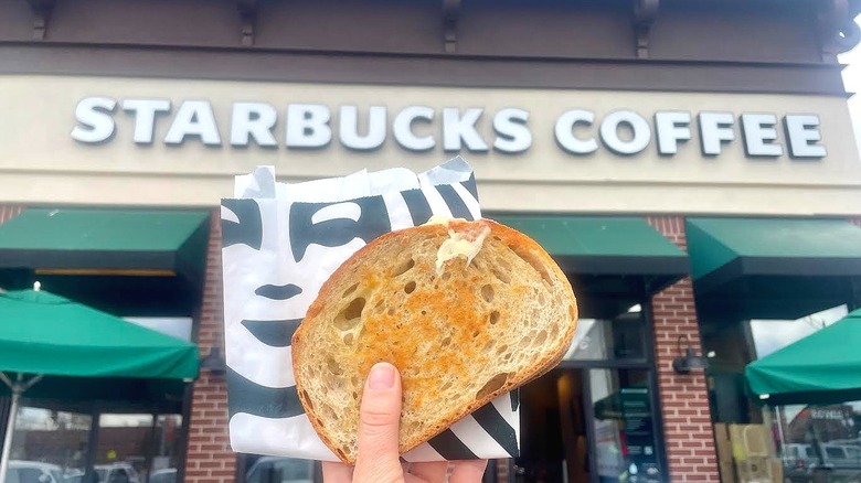 Hand holding Starbucks' Grilled Cheese in front of store