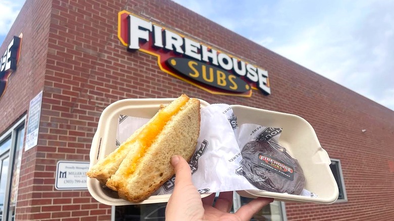 Hand holding Firehouse Subs' Hot Grilled Cheese Combo in front of store