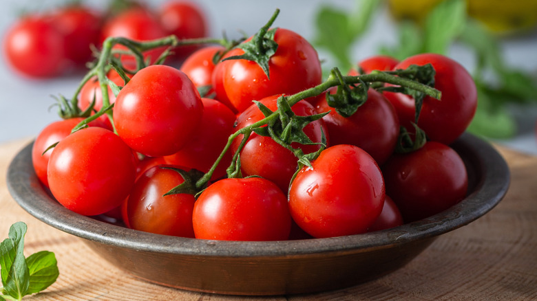 Fresh cherry tomatoes sit in a dish on a wooden board.