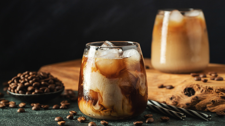 A glass of iced coffee with milk and coffee beans around it