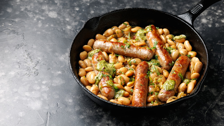 Lima beans in a cast iron pan with whole sausages