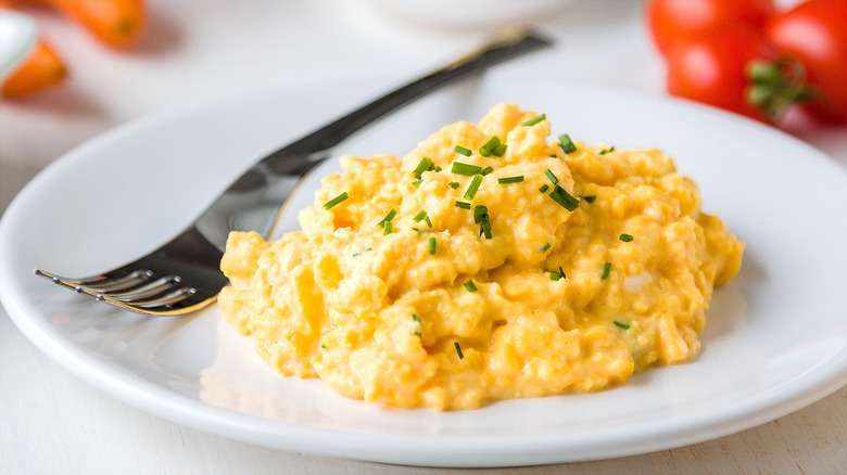 Soft scrambled eggs with fresh chives on a white plate with a metal fork