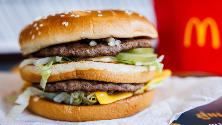 McDonald's Big Mac hamburger with visible onion, beef patties, pickles, lettuce and cheese on a three layered sesame seed bun with French fries