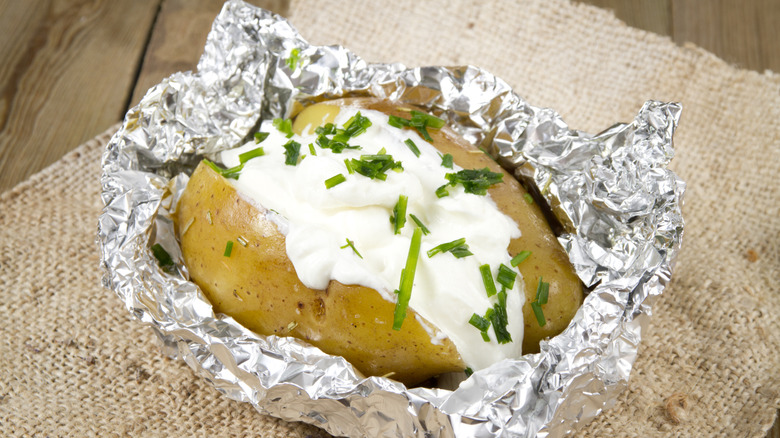 Baked potato with a creamy center topped with chives and half covered in aluminum foil