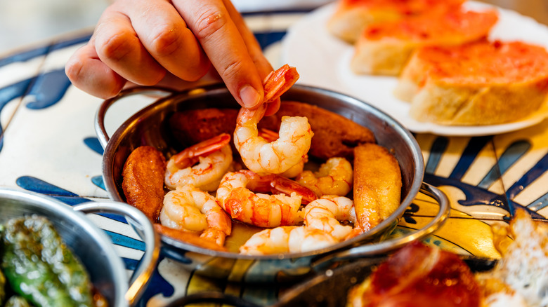 Person picking up cooked shrimp from a small metal bowl