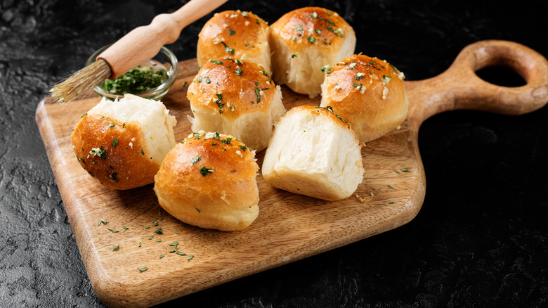 Dinner rolls improved with garlic and herbs are arranged on a wooden board.