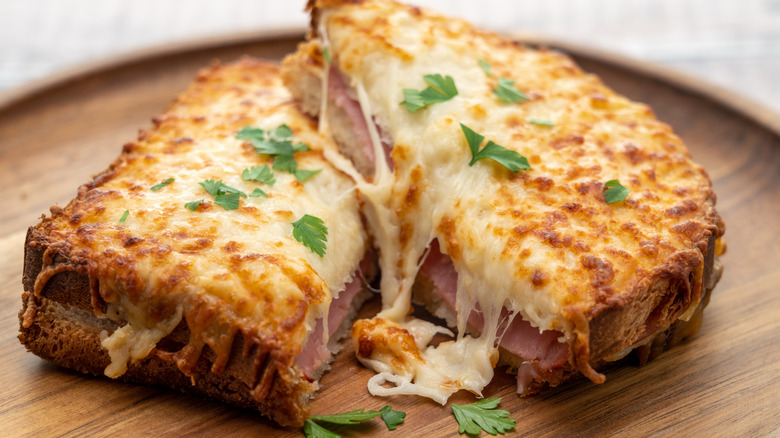 A croque monsieur on a wooden board with parsley garnish