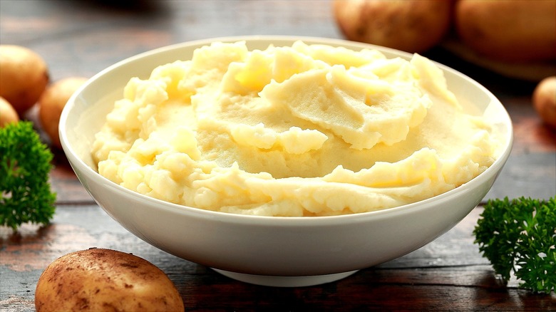 Mashed potatoes in a cream-colored serving bowl on a wooden table