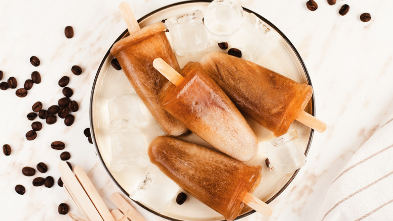 Coffee popsicles on plate with black trim on marble counter top with scattered coffee beans