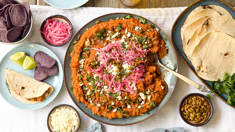 Refried Mayocoba beans on serving platter with garnishes, tortillas, and chips