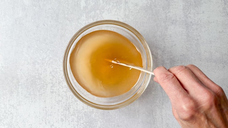 Stirring brine for pickling onions in a small glass bowl with wooden spoon