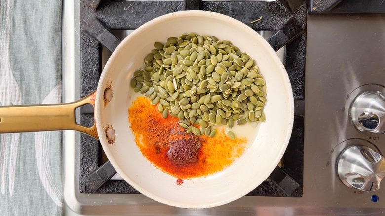 Raw pepitas and chile oil ingredients in skillet on stovetop