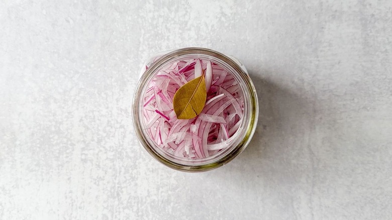 Sliced red onion and a bay leaf in a glass jar top view
