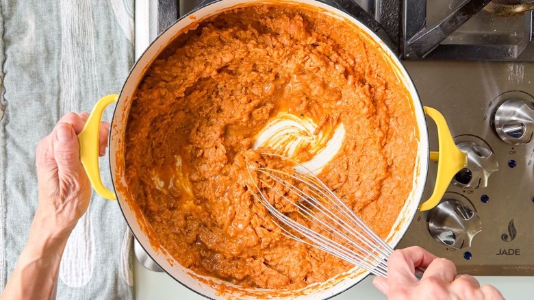 Whisking lime juice and cooking liquid into refried Mayocoba beans in Dutch oven