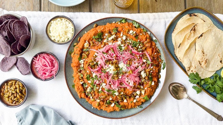 Refried Mayocoba beans on serving platter with garnishes, tortillas, and chips