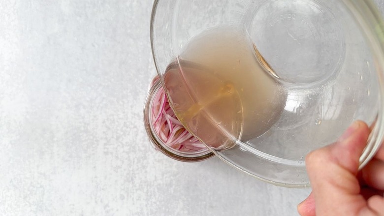 Pouring brine over sliced onion and bay leaf in glass jar