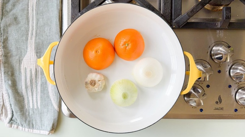 Halved orange, white onion, and garlic head cut-side-down in yellow Dutch oven