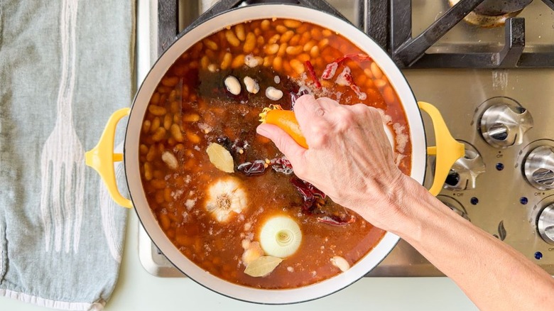 Squeezing charred orange into pot with Mayocoba beans and chiles