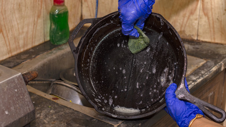 An individual scrubbing a cast-iron pan in the dishwasher.