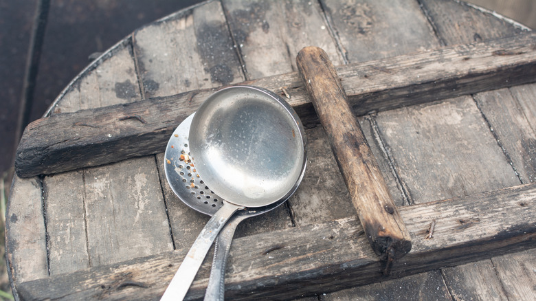 A metal skimmer and ladle sitting on a wooden surface
